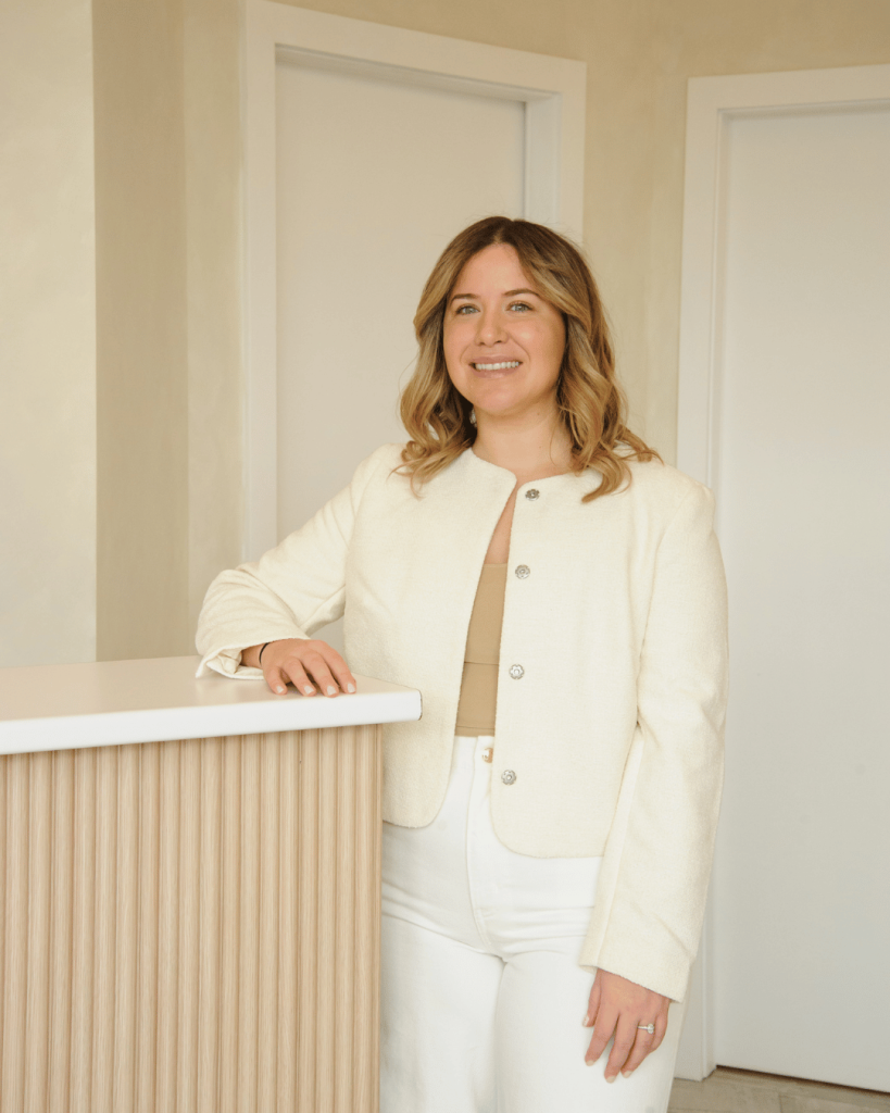 Smiling woman standing behind a spa reception desk — welcoming guests to a boutique spa experience.