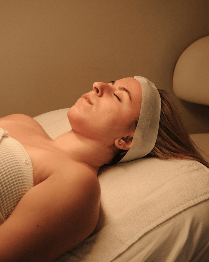 Woman lying down on spa bed mid-treatment, looking peaceful — reflecting the calm of holistic facial therapy.