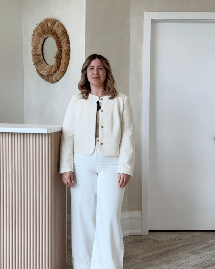 Professional woman standing in front of spa reception desk — embodying warmth and personalized client care.